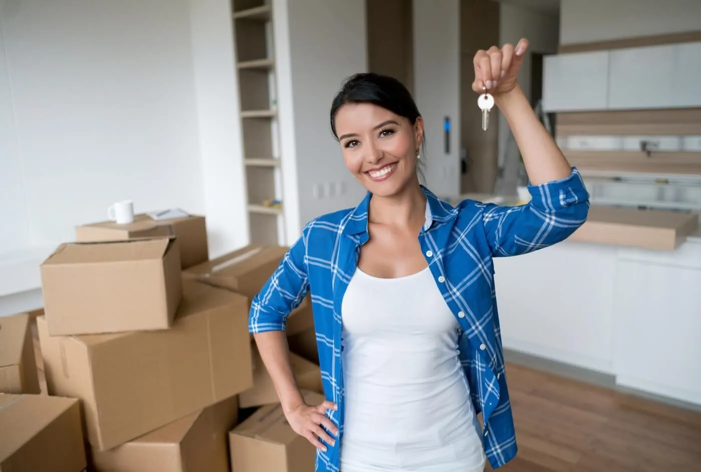 Photo of a smiling woman holding the keys in her new apartment, moving boxes on the background