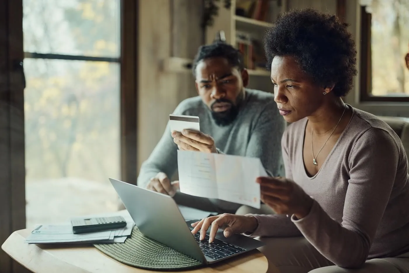 Concerned couple using a credit card and a laptop to pay bills at home