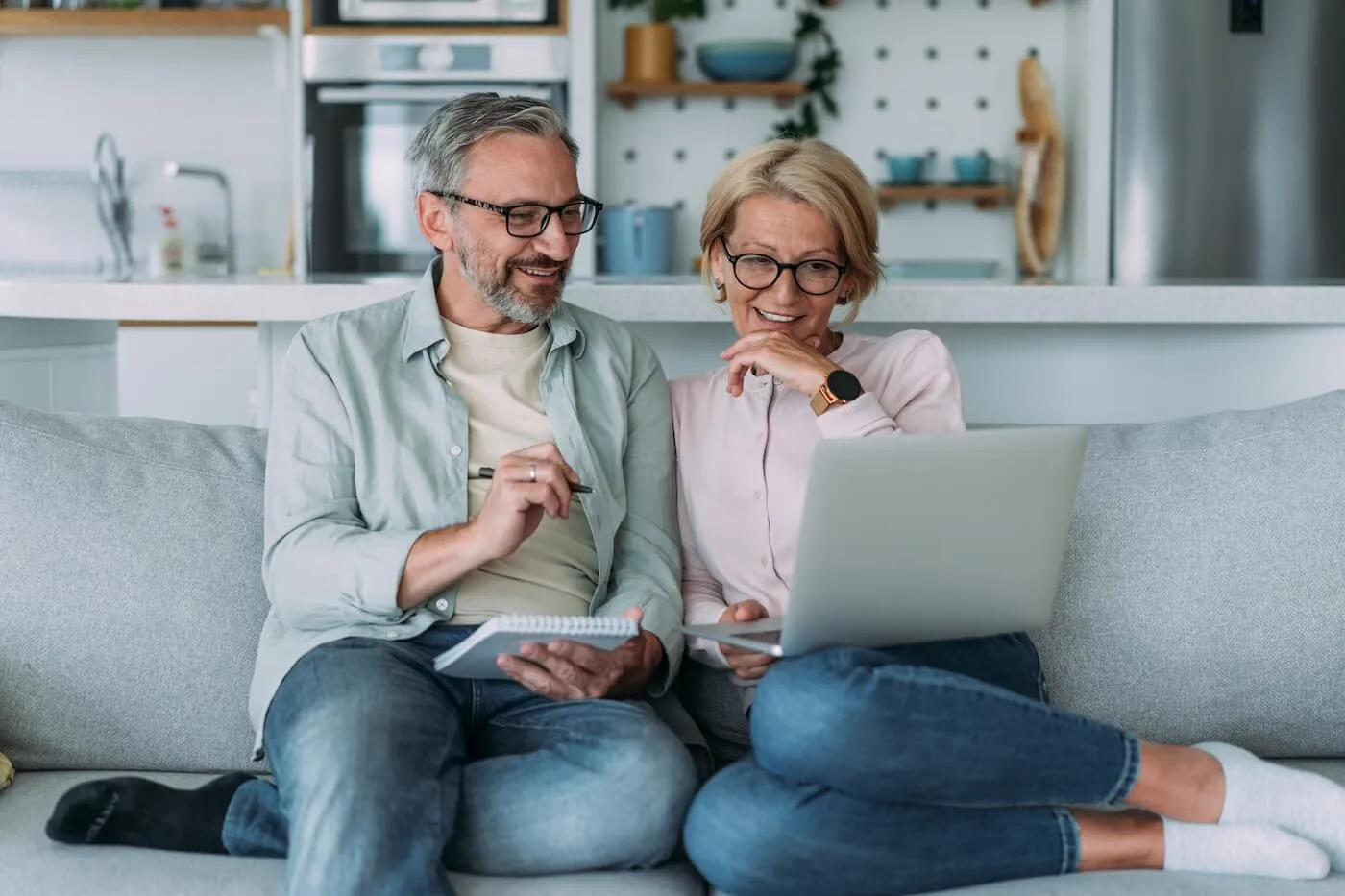 Mature couple sitting comfortably on the sofa with a paper pad and a laptop while planning finances
