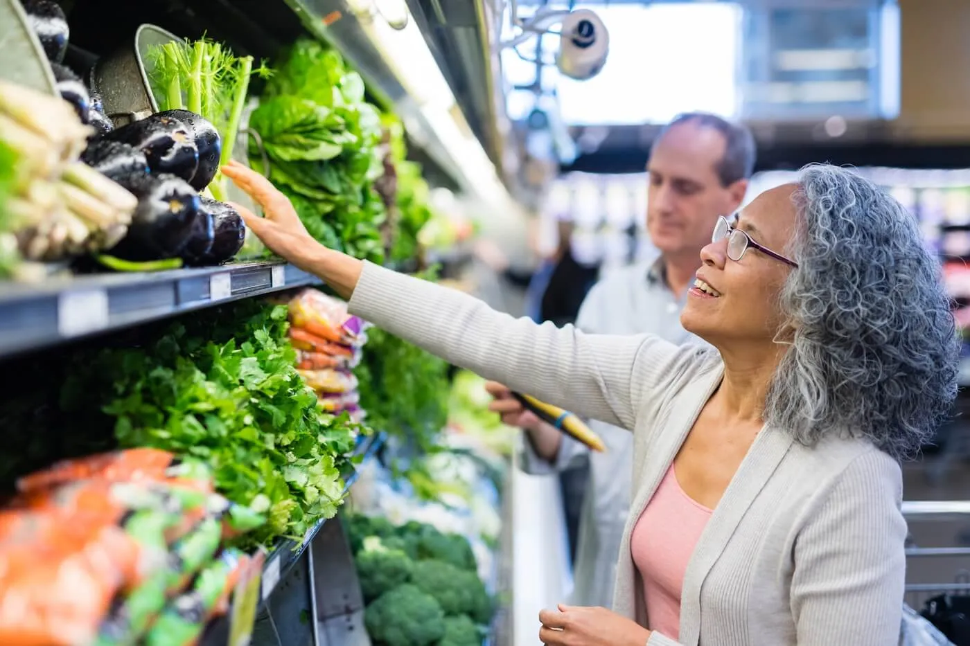 Senior woman choosing the greens in the grocery store, a mature man is shopping on the background