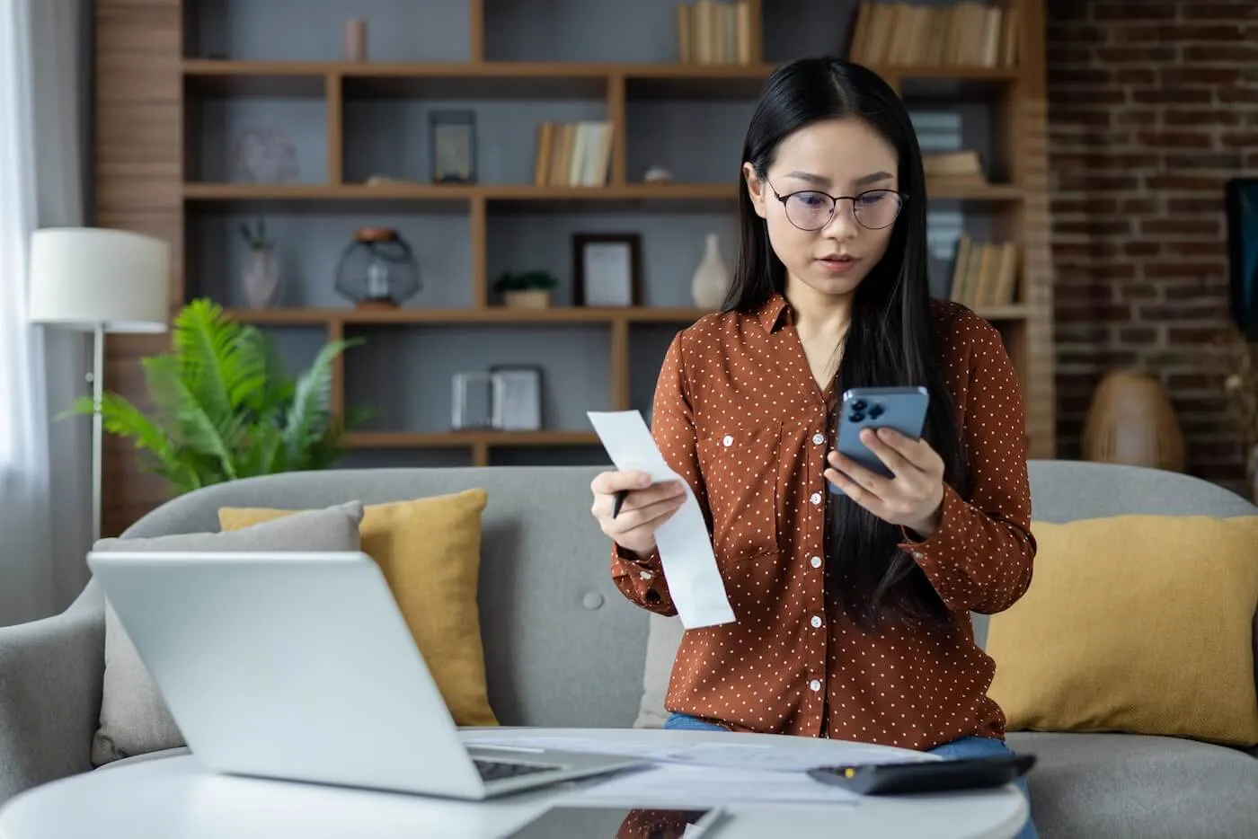 Young woman calculating her spendings on a smartphone at home