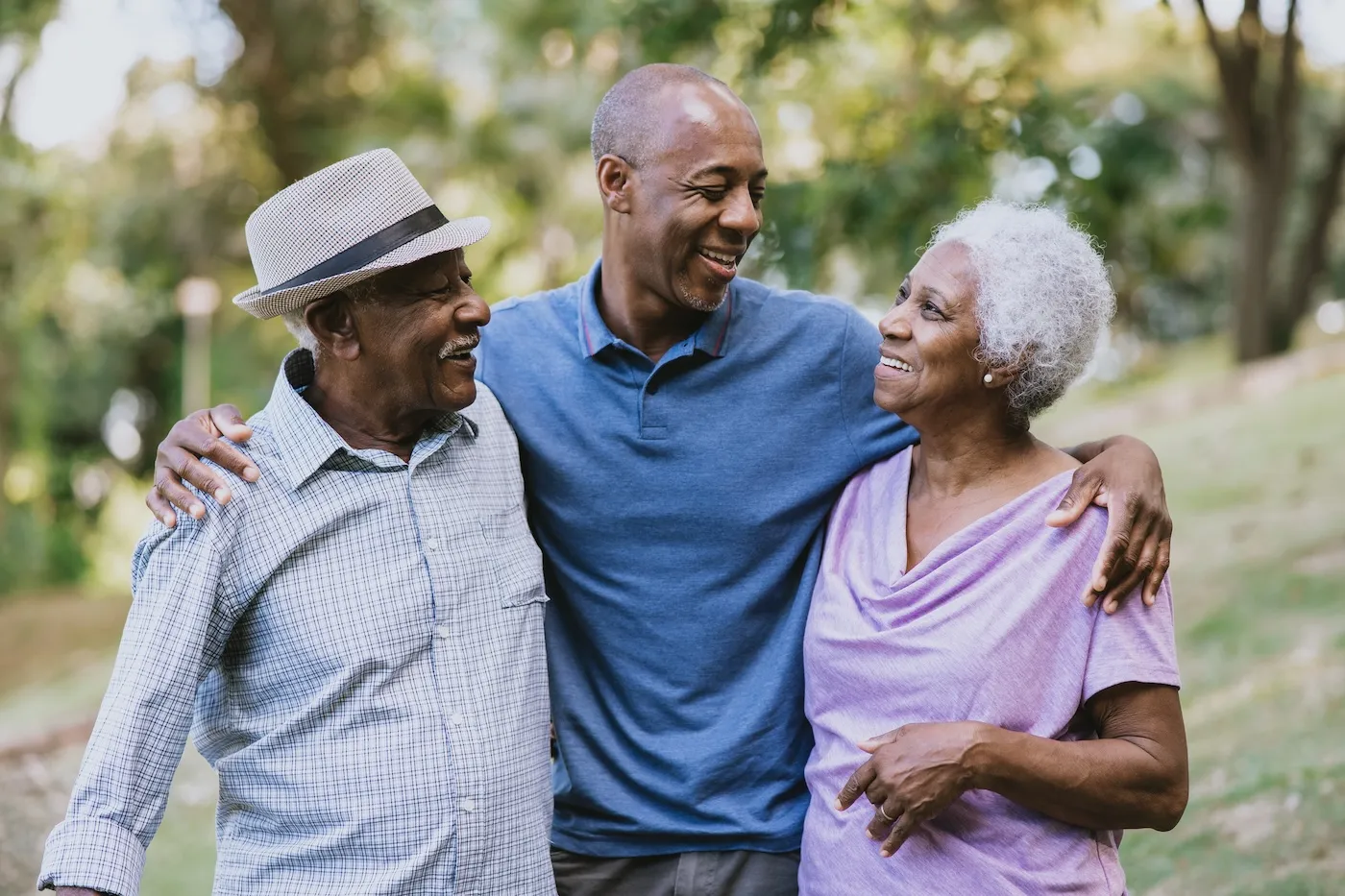 Smiling mature man walking outdoors with his elderly parents, gently embracing them