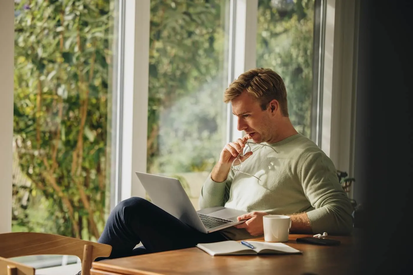 Focused mature man working on his laptop next to a window with a coffee mug beside him