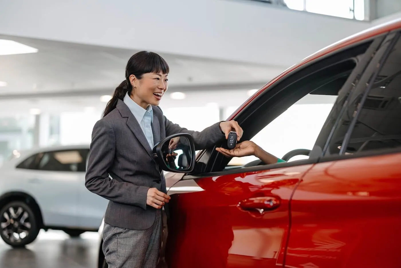 Smiling female agent giving the keys to a buyer of a red car