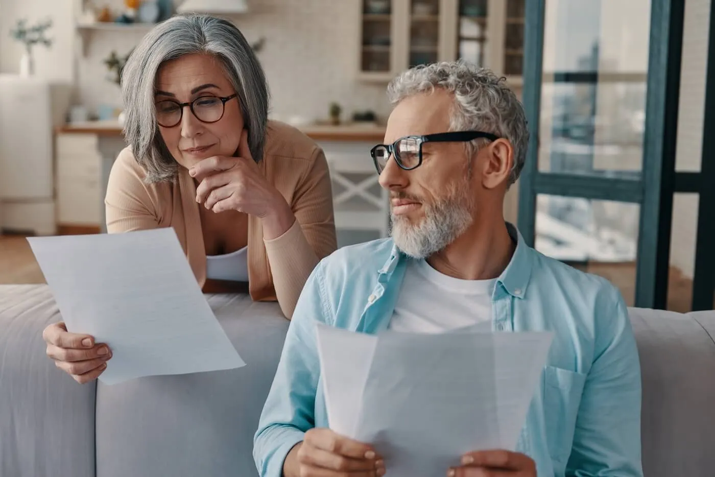 Focused senior couple reviewing printed documents at home
