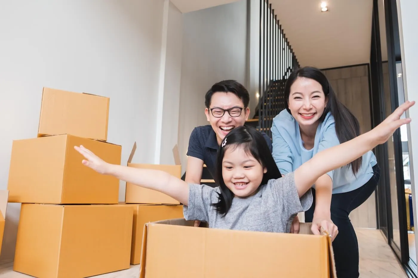 Happy family with a young girl playing with the moving boxes in their new house.