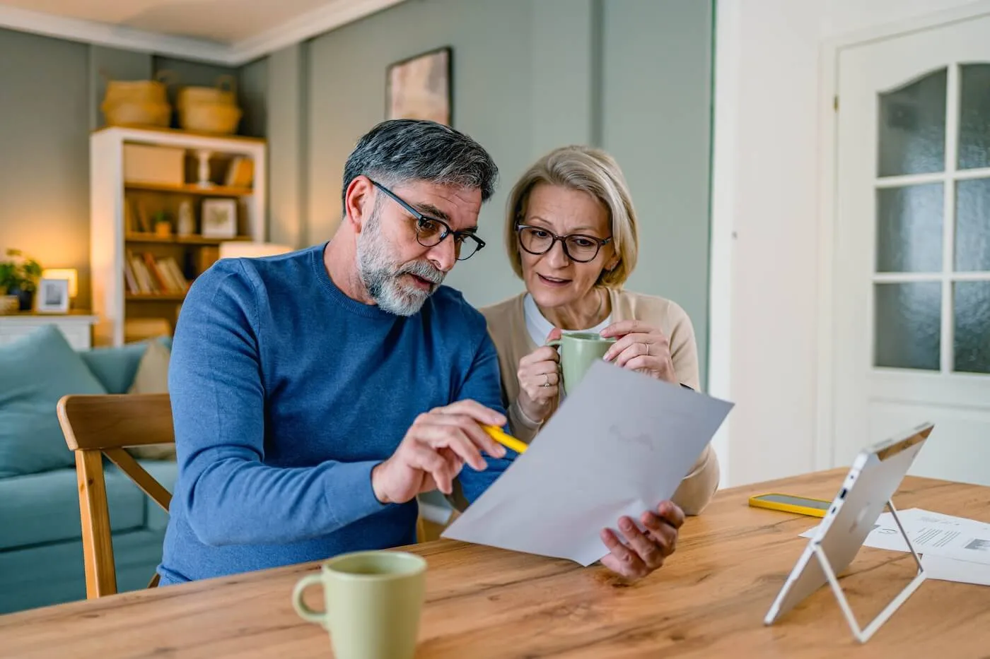 Mature couple sitting together, reviewing printed documents while enjoying hot drinks in a cozy home setting