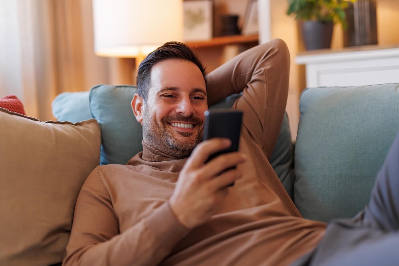 Smiling relaxed man lying on the couch with a smarphone