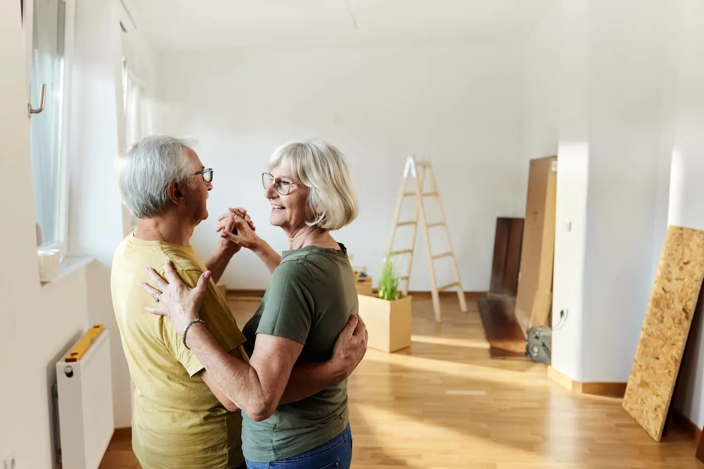 Senior couple dancing in their new living room, a leader and moving boxes on the background