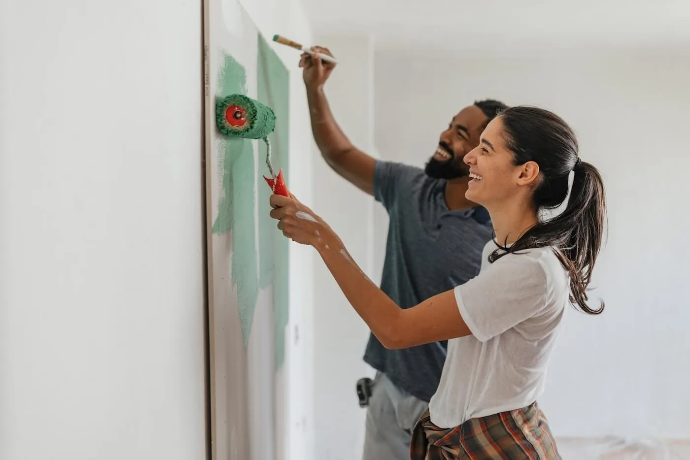 Smiling young couple examining green paint swatches on a wall panel.