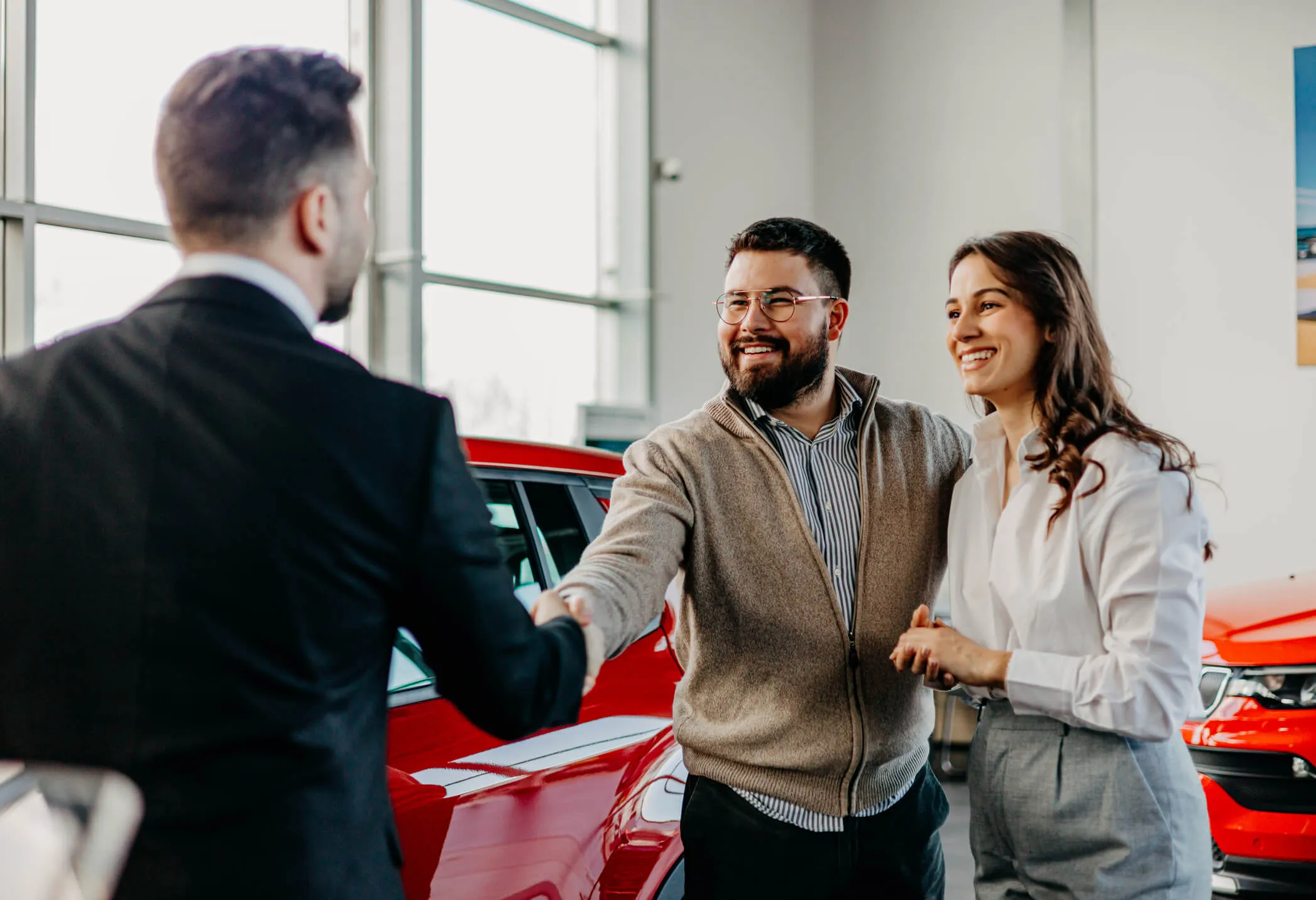 Happy couple shaking hands with the male sales agent in the car dealership