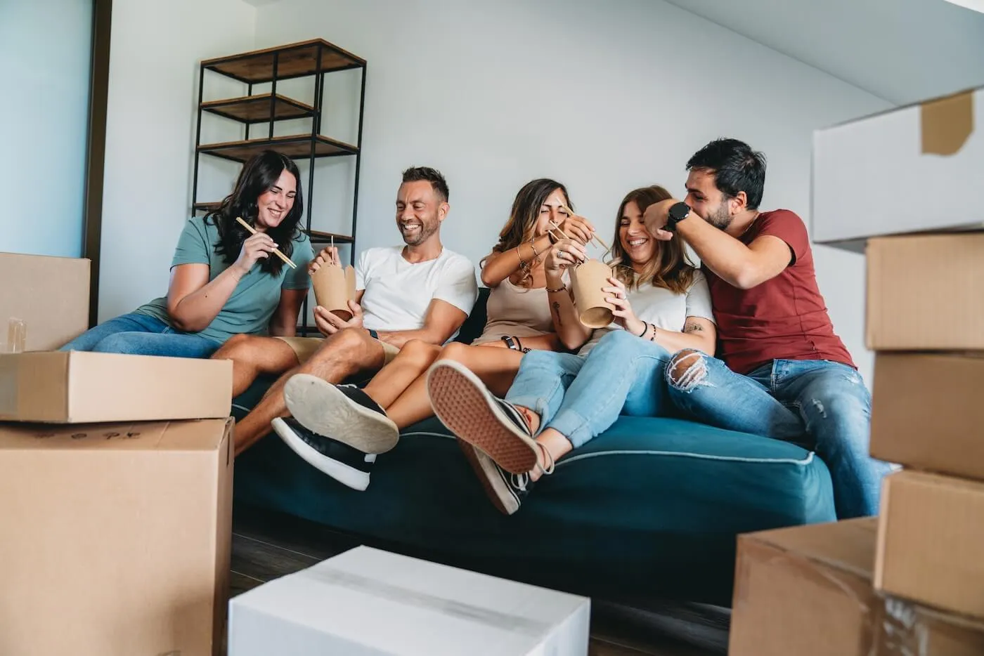 A cheerful group of friends having lunch on a couch surrounded by moving boxes