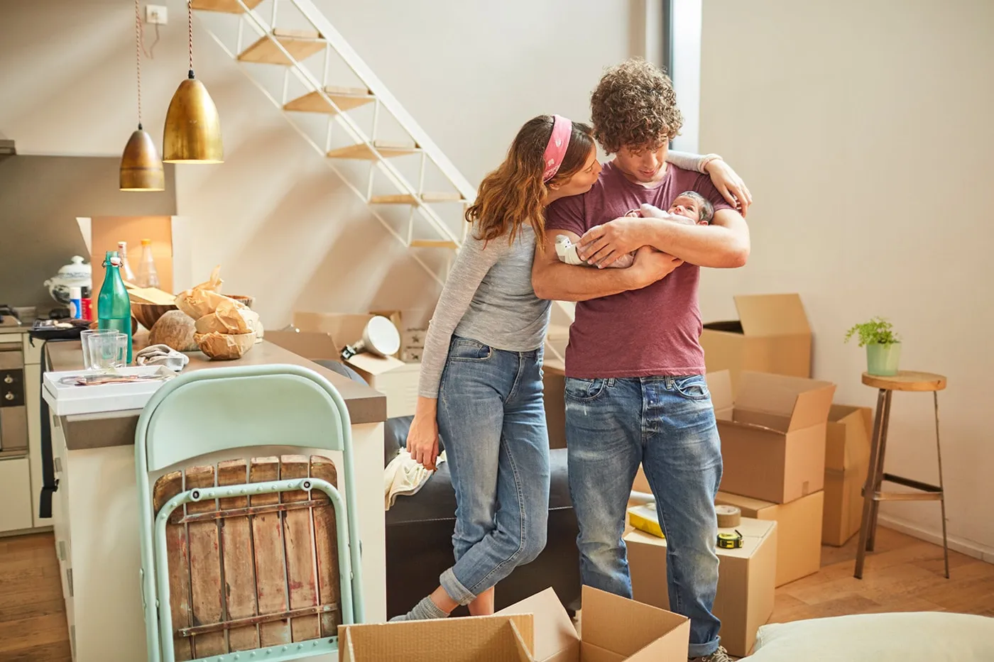 Young parents holding their baby while standing in a living room full of moving boxes