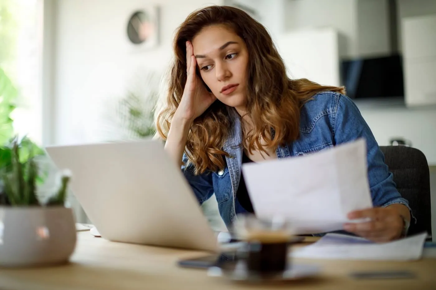 Worried young woman reviewing documents while staring at her laptop screen