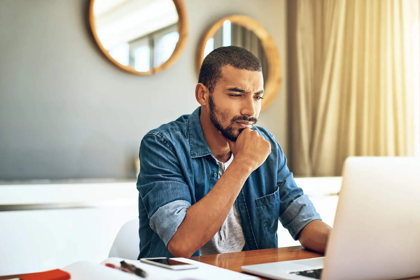 Pensive young man looking up online what to do when bank is acquired.