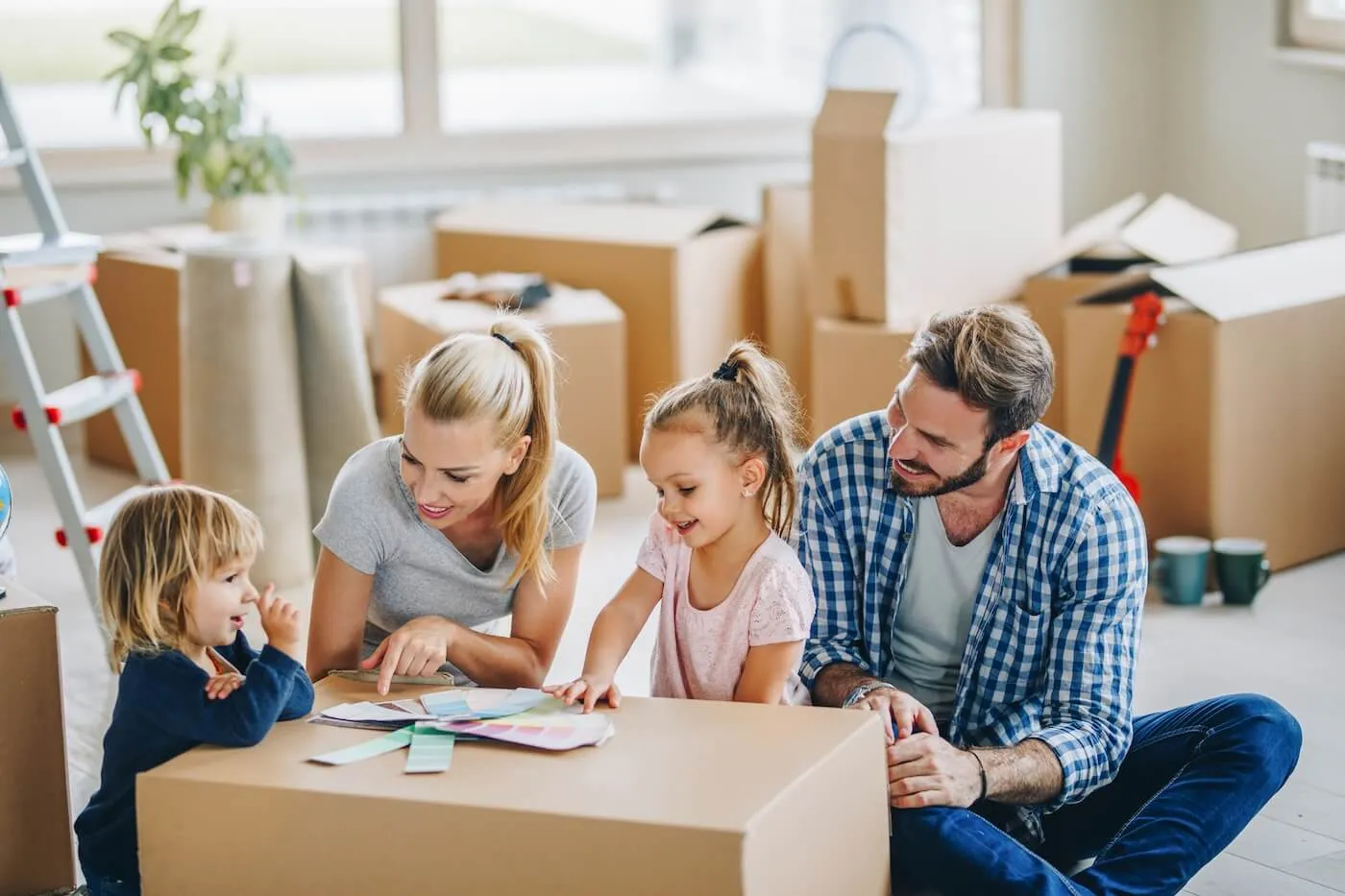 Family of four sitting on the floor of the new living room surrounded by moving boxes and choosing the wall paint color