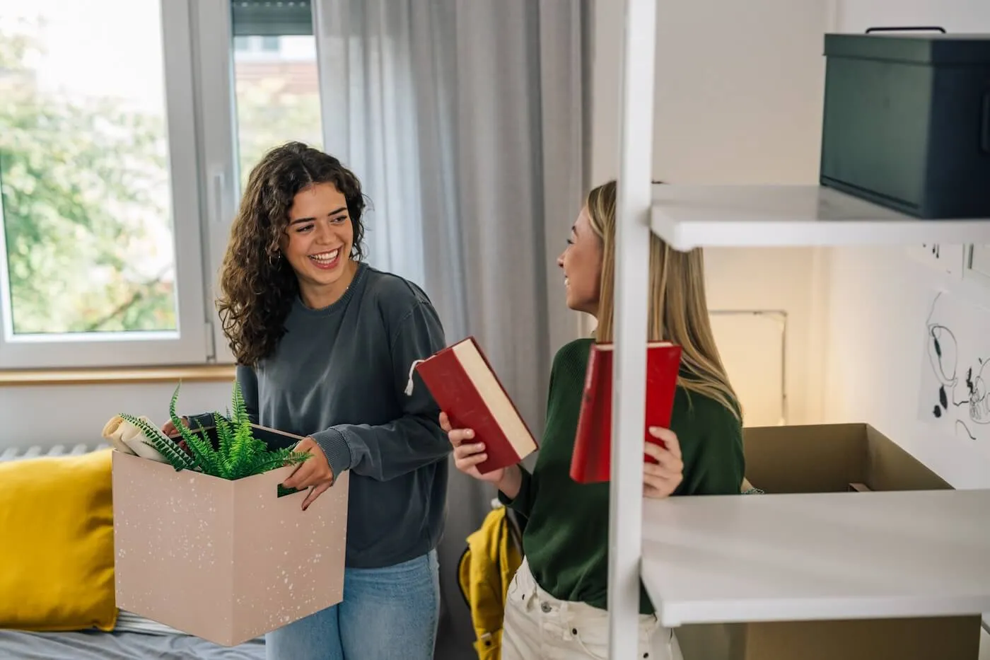 Two smiling female students organizing their dorm room together