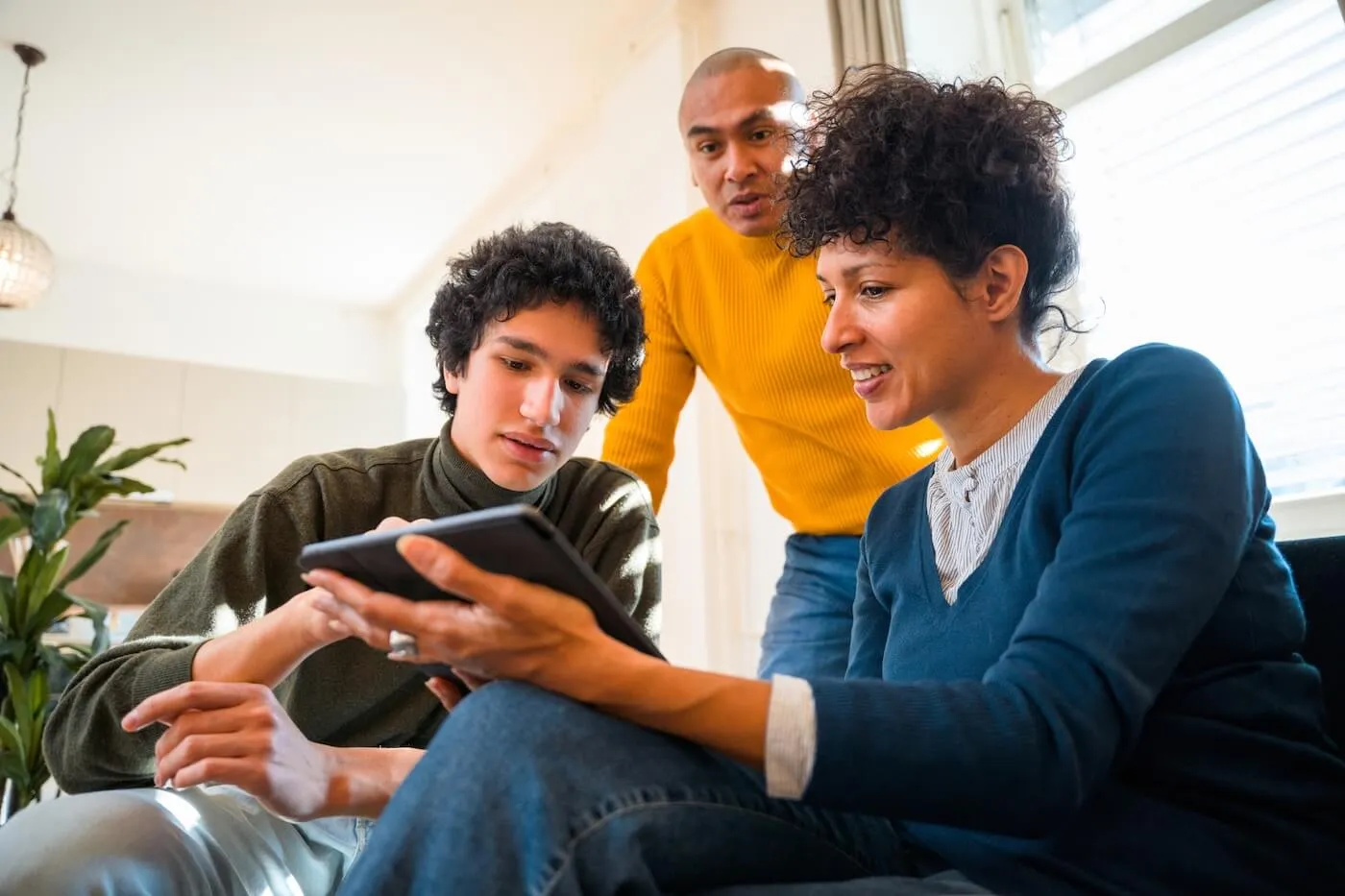 Mother and teenage son exploring a mobile banking app on a tablet, while the father stands behind them