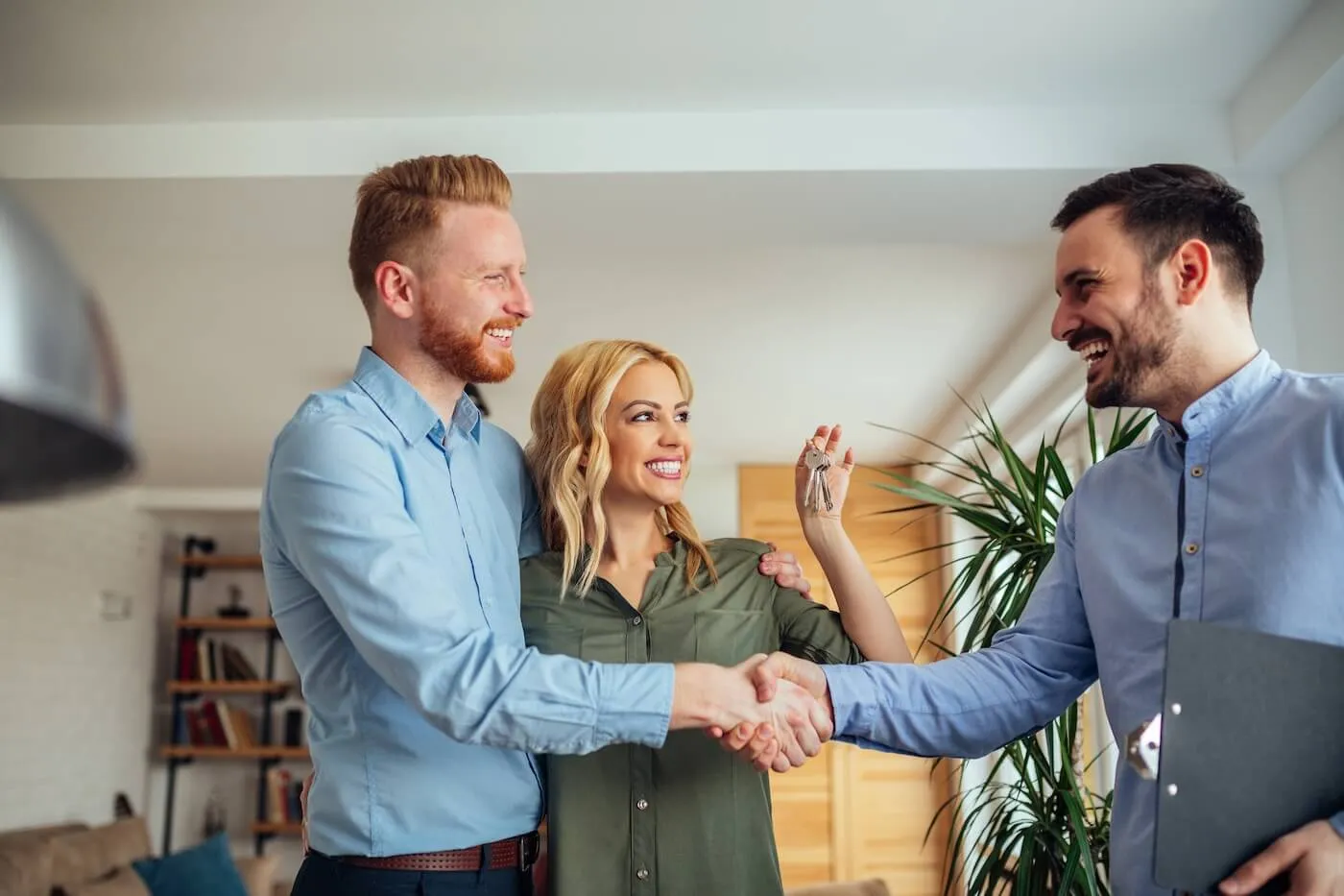 Smiling man shaking hands with the happy couple after renting out his house, a woman is holding the keys
