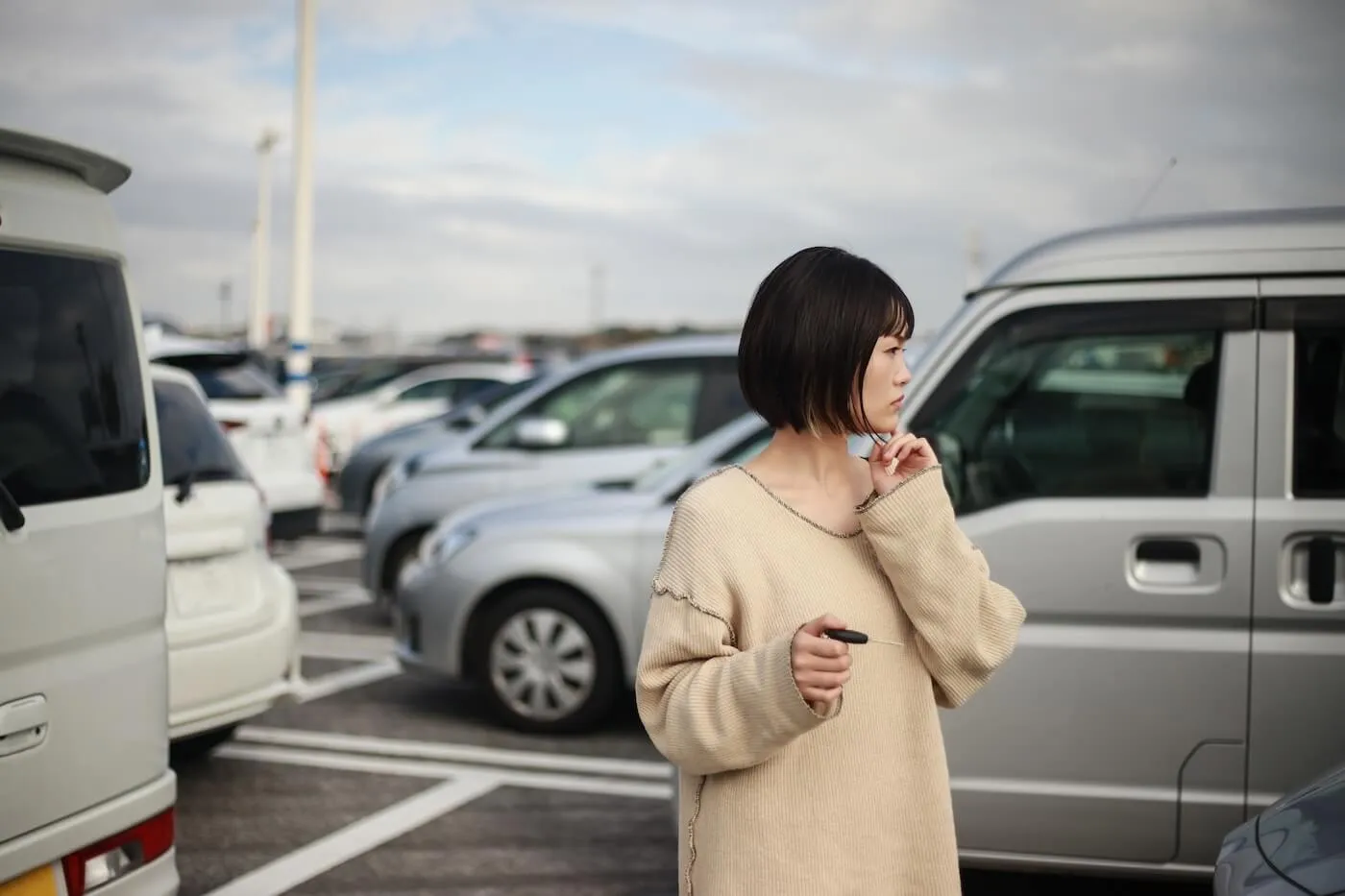 Concerned young woman using car keys to find her car in the parking lot