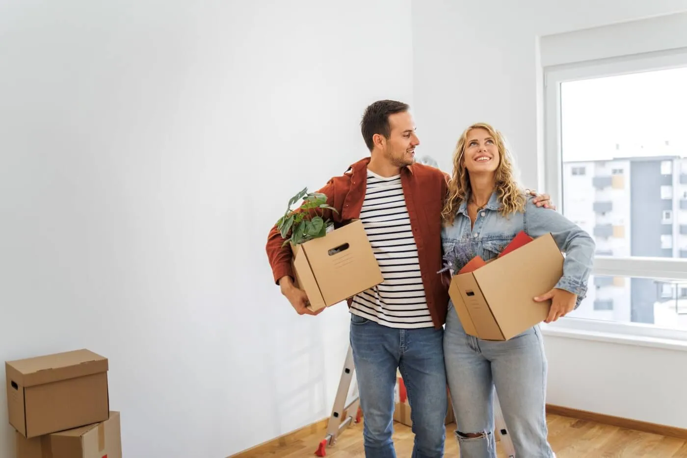 A couple moving in to their new home, holding moving boxes.