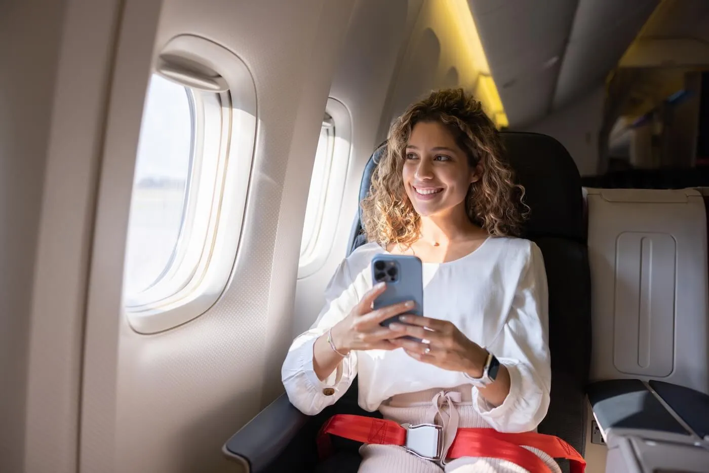 Smiling woman sitting in the plane with the smartphone in her hands