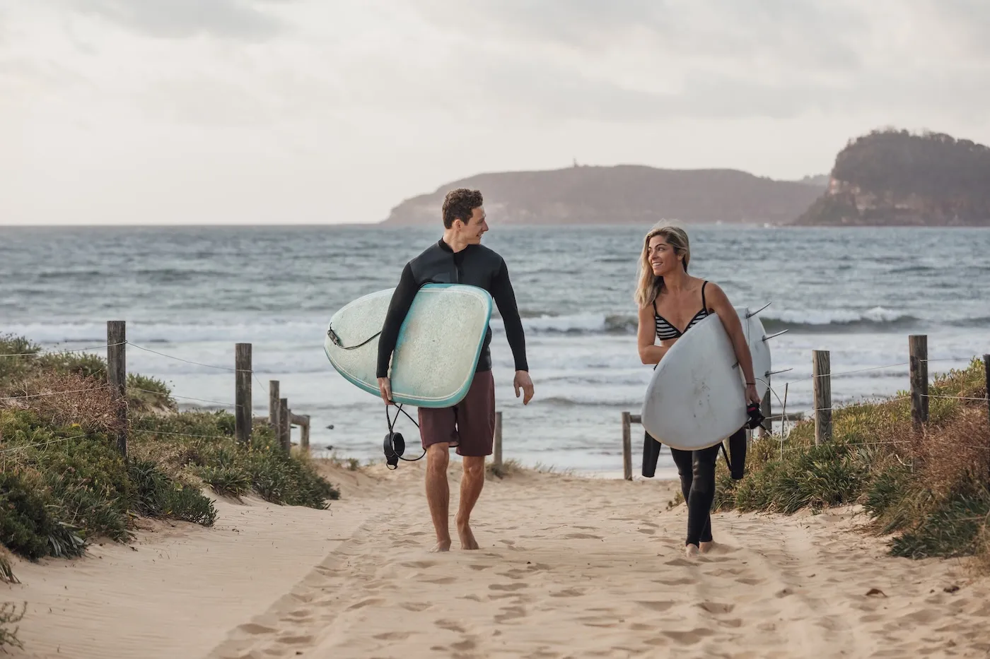 A front-view shot of a young man and woman holding a surfing board on a beach in Sydney, Australia.