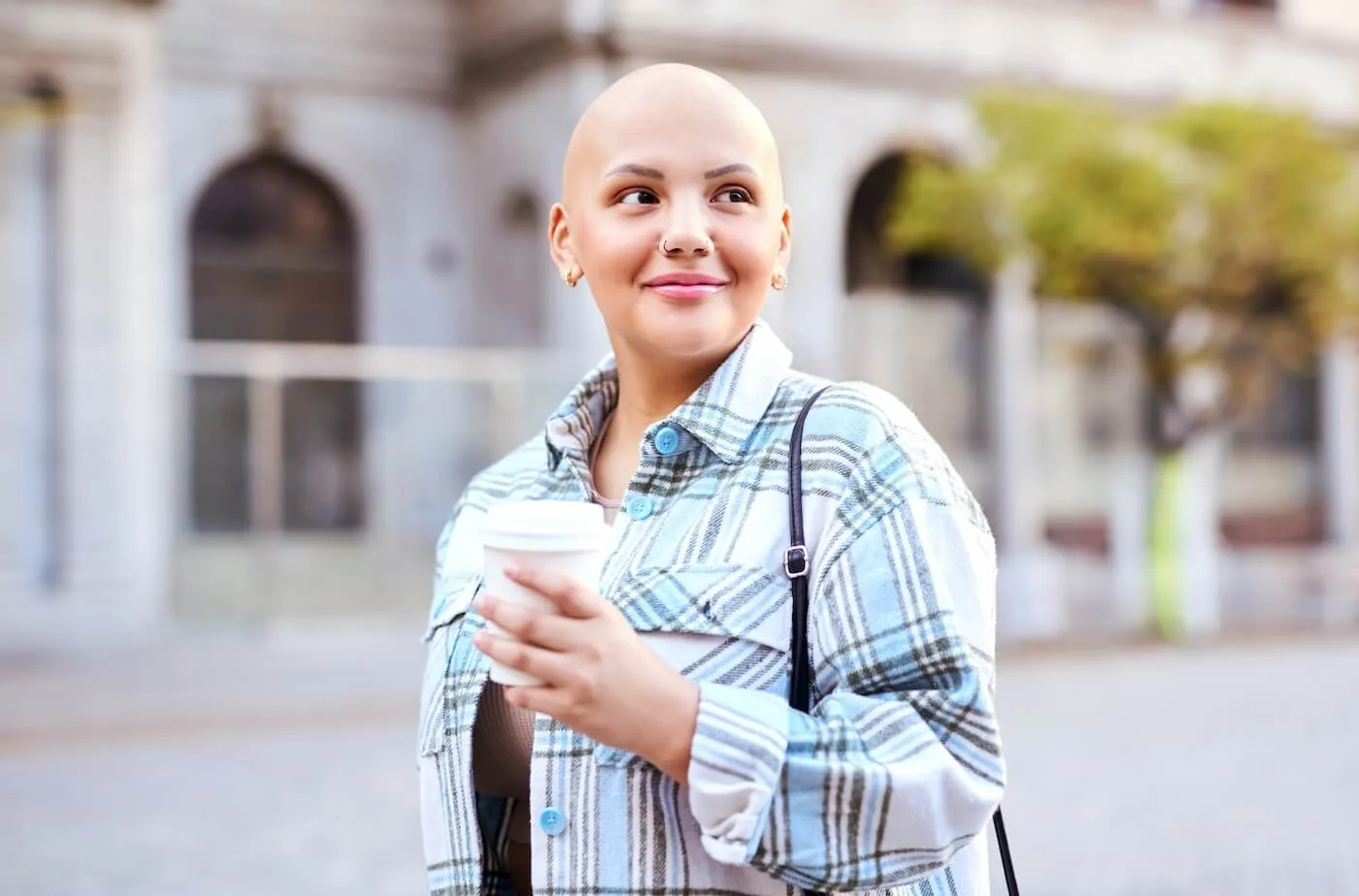 Smiling young woman with a shaved head enjoying a city stroll with a cup of coffee.