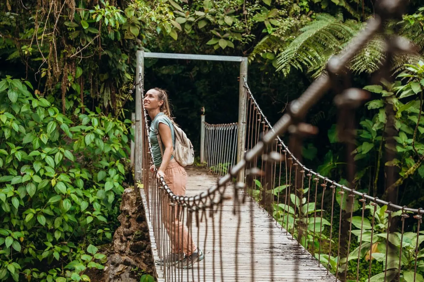 Young woman with a backpack enjoying a hike on a suspension bridge surrounded by lush jungle