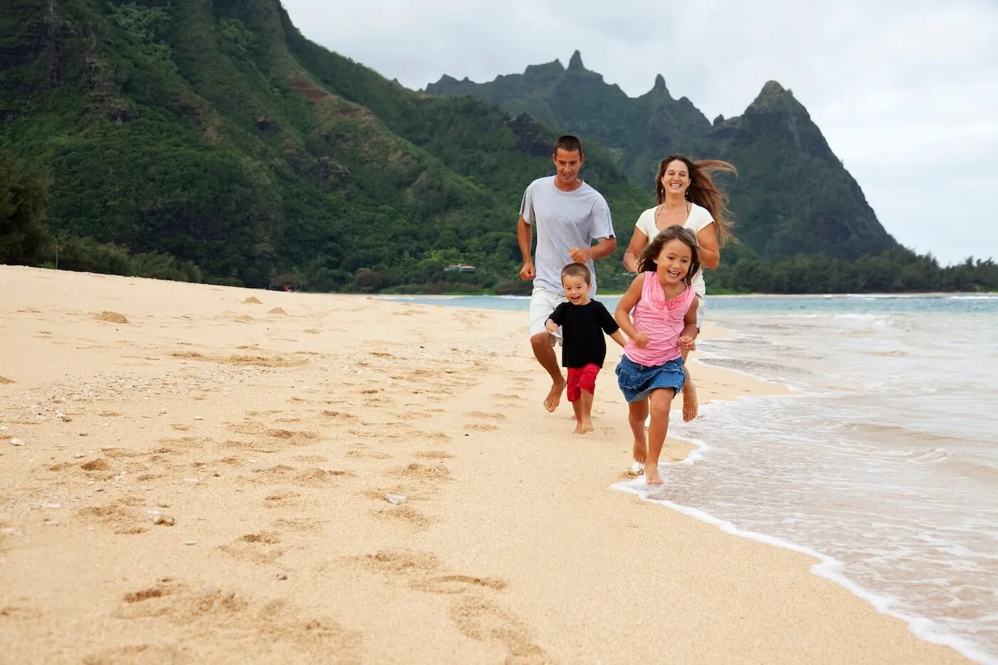Happy family with two young kids running on the Tunnels Beach, HI, in a warm cloudy day