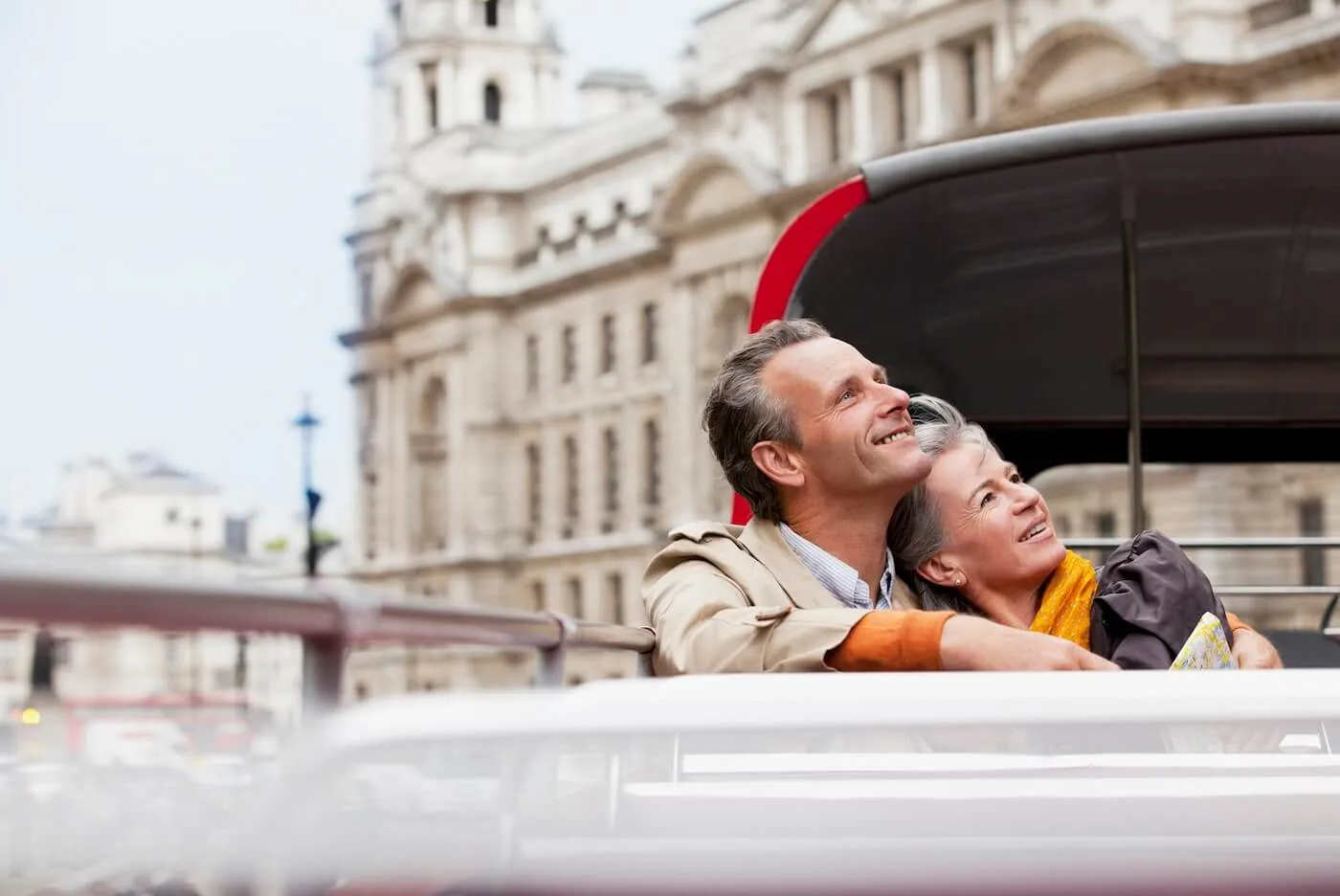 Happy senior couple sitting on a London double-decker bus, admiring the city's historic architecture