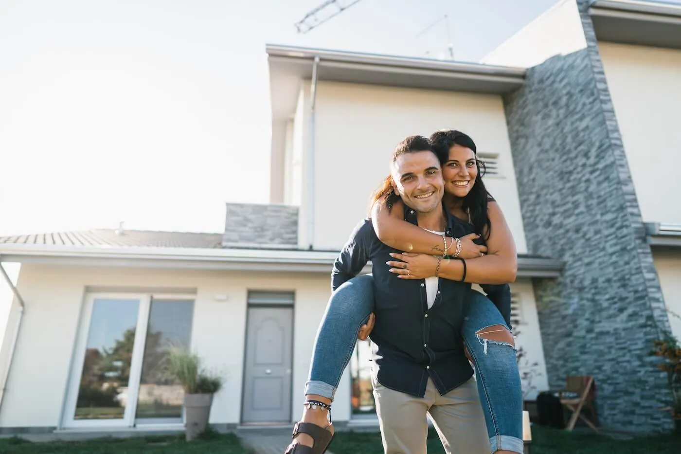 Happy young couple standing in front of the house, the woman piggybacks the man
