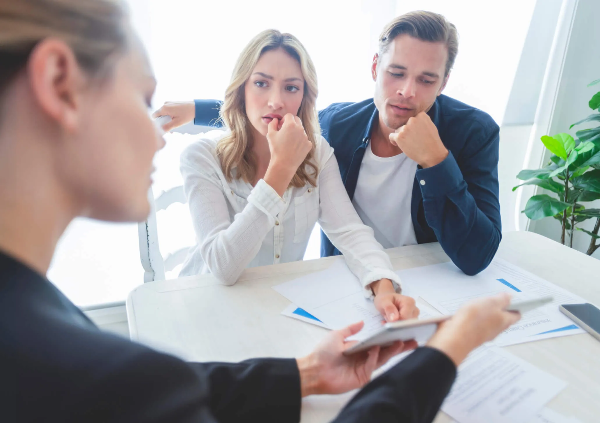 Concerned young couple talking to a female real estate agent who is showing something on a tablet