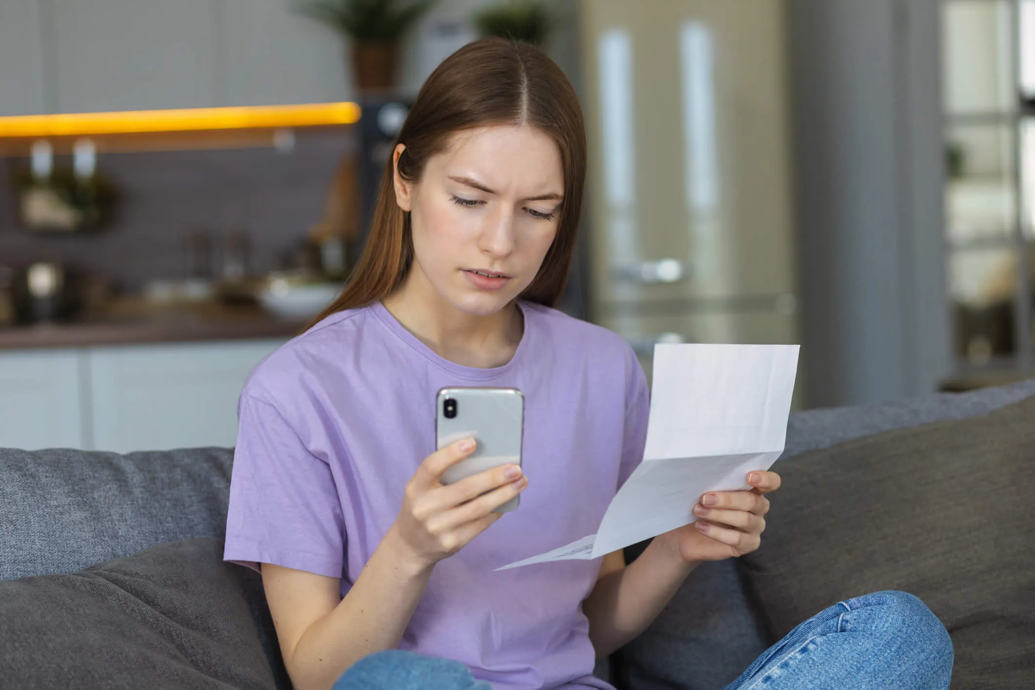 Concerned woman checking her mobile phone while holding a letter