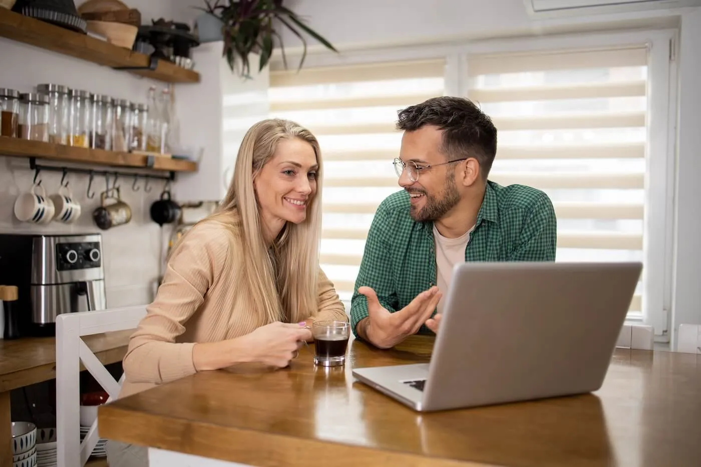 Happy couple discussing home insurance while using a laptop and enjoying a cup of coffee