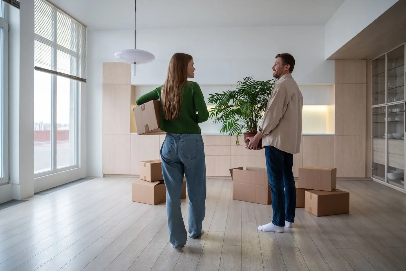 Young couple moving into a new apartment, carrying cardboard boxes with belongings, potted plants