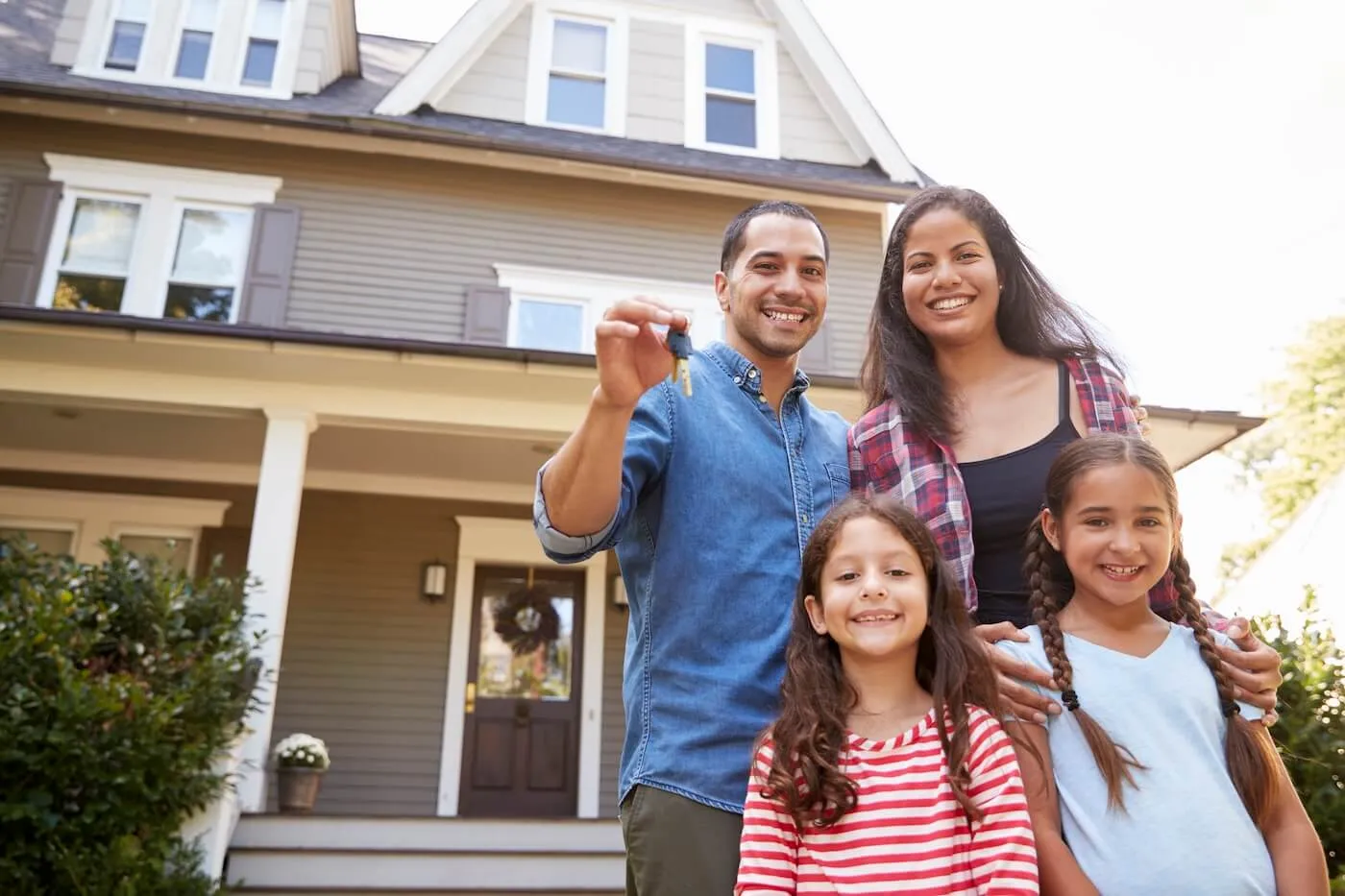 Portrait of family of four holding keys to new home on moving in day