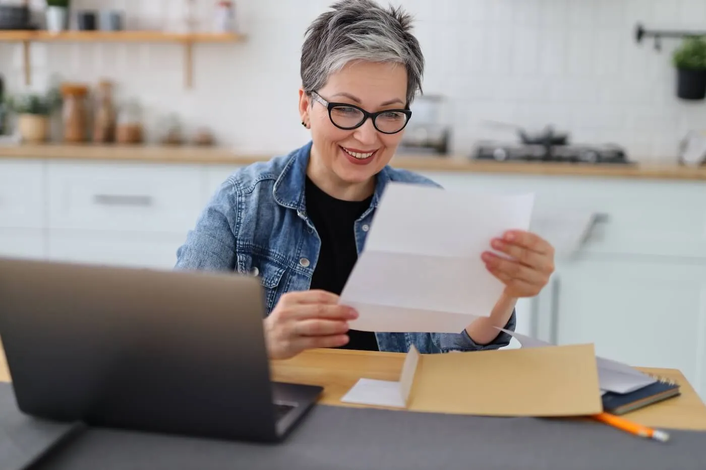 Mature woman reading her mail while using her laptop at home.