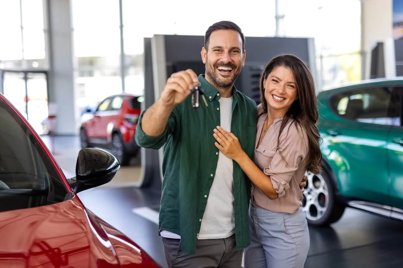 Happy couple standing inside a car dealership, proudly holding the keys to their new car