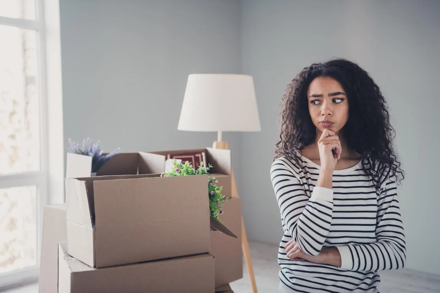 Photo of a concerned young woman standing in an empty room next to the moving boxes