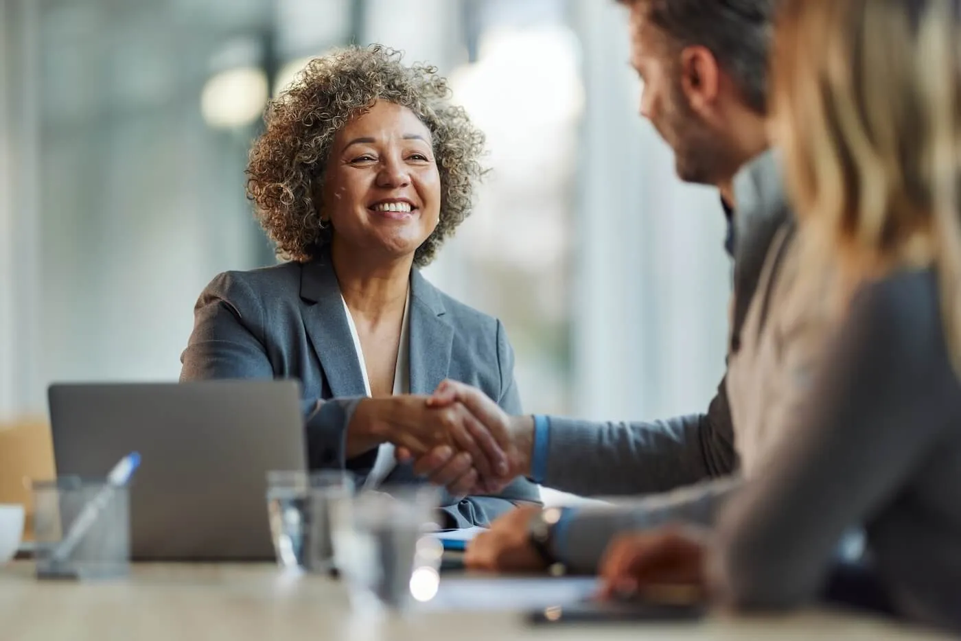 Female real estate agent, a mature smiling woman, shaking hands with the male customer; his female partner sitting next to him