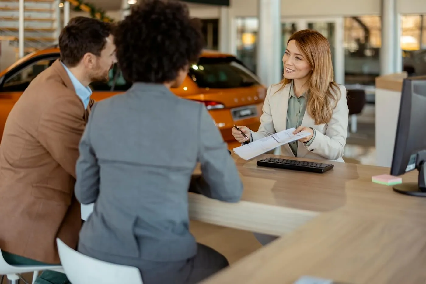 Smiling saleswoman explaining the contract terms to a couple in the car dealership