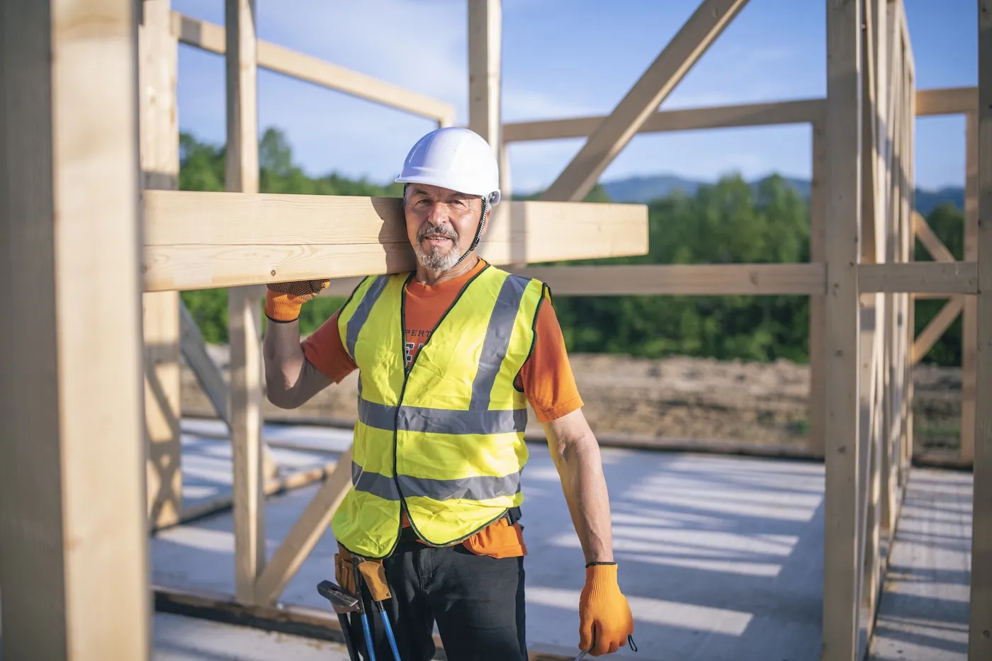 Portrait of male worker on construction site holding plank beam on his shoulder.