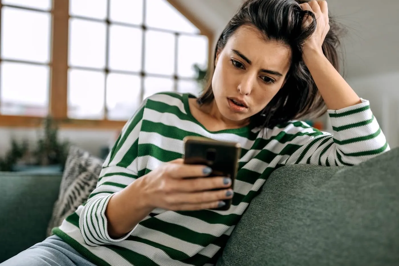 Concerned young woman sitting on the sofa and looking at her smartphone