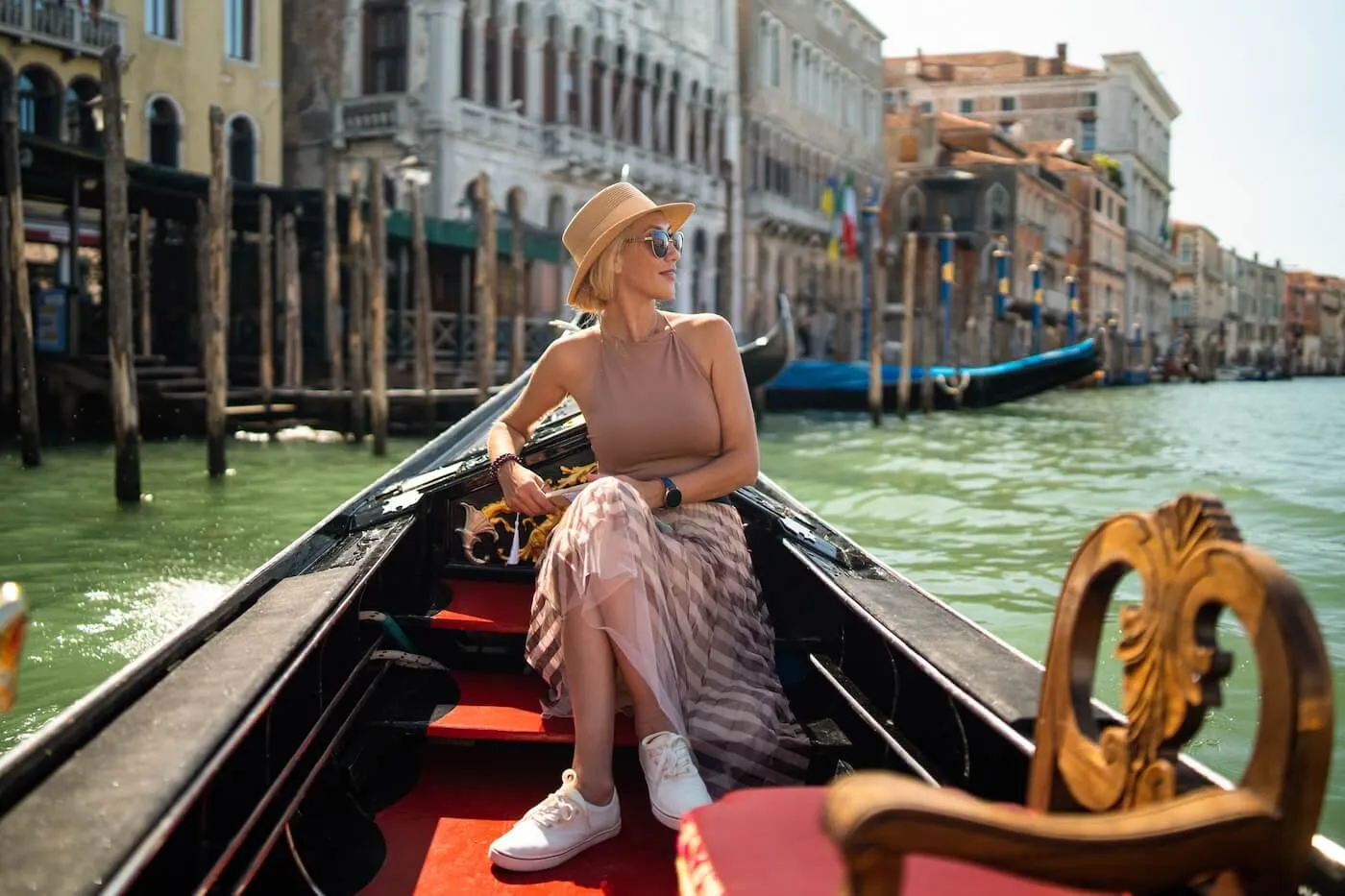A relaxed woman in a summer outfit sitting in a gondola in Venice on a sunny day