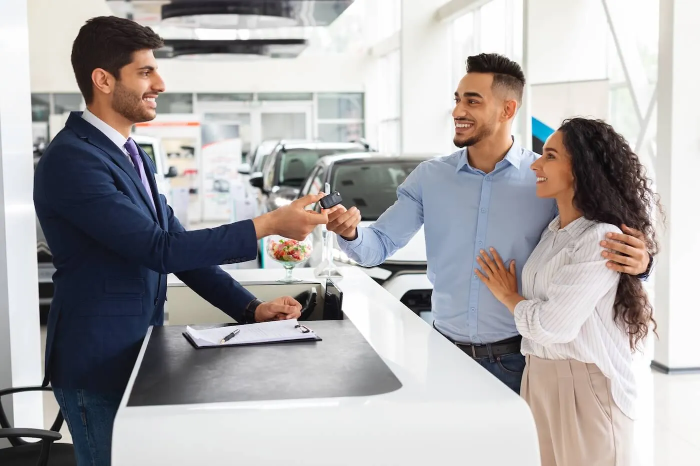 Happy young couple taking the car keys from the smiling dealership agent