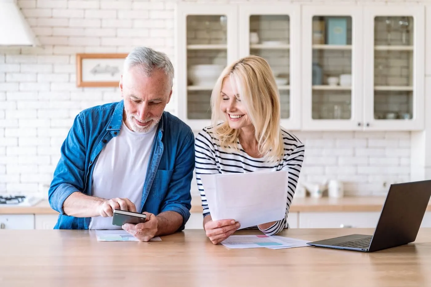 Mature couple reviewing finances at home, with a laptop beside them