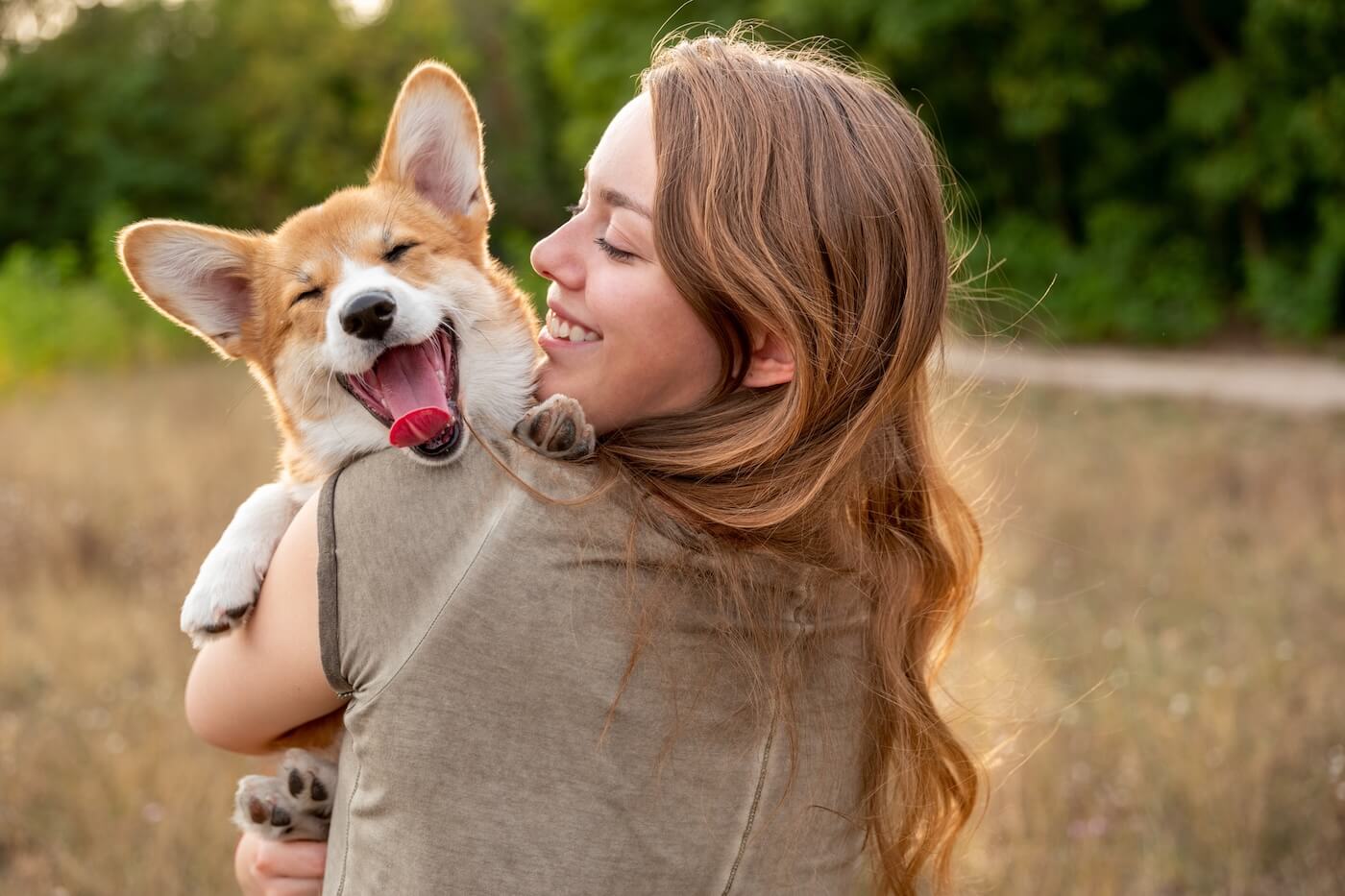 Smiling young woman holding a corgi puppy in the park