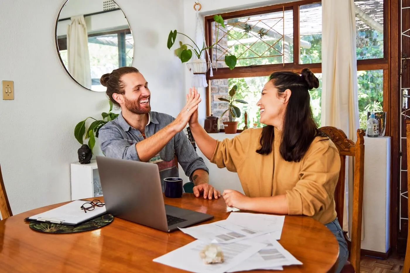 Happy young couple giving high five while calculating finances at home