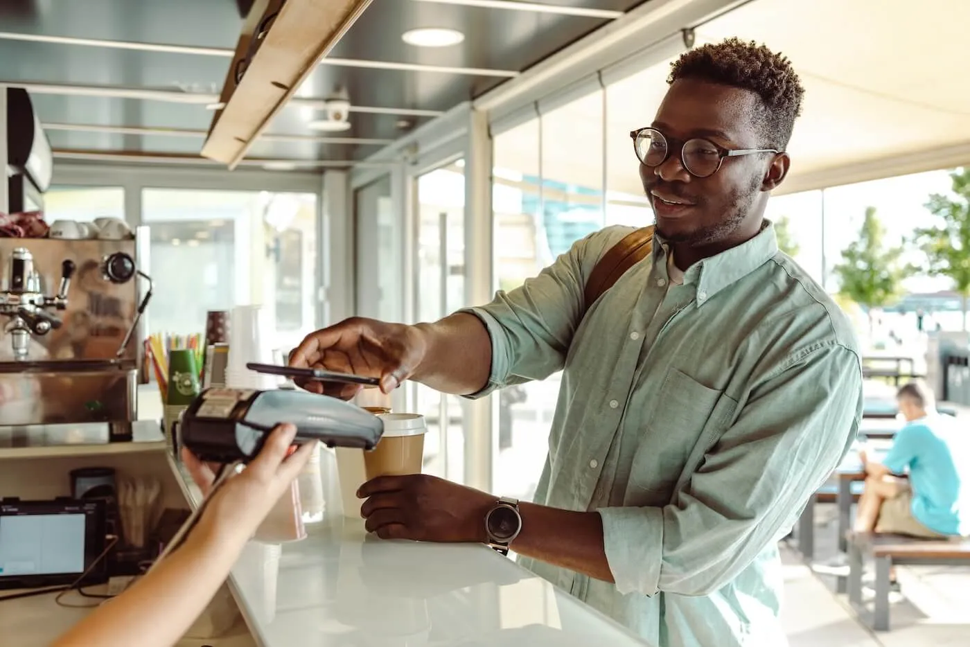 Young man using his smartphone to pay for coffee at a cafe